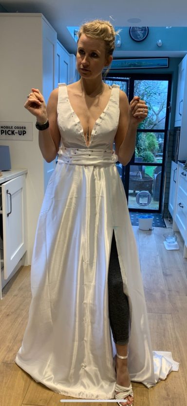 Woman in a white dress with a thigh-high slit, striking a playful pose in a kitchen.