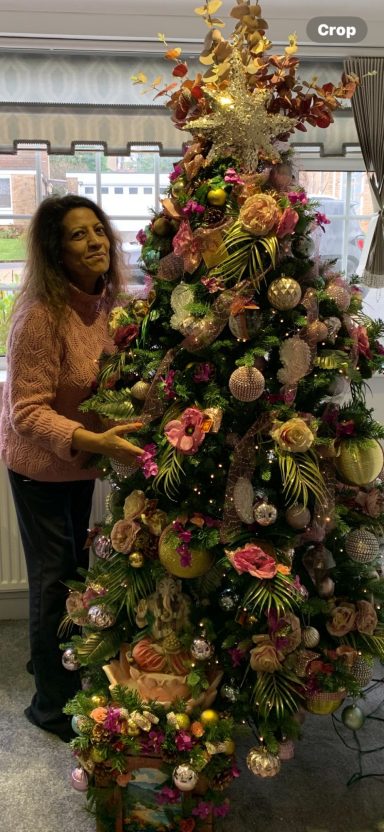 A woman stands beside a beautifully decorated floral Christmas tree.