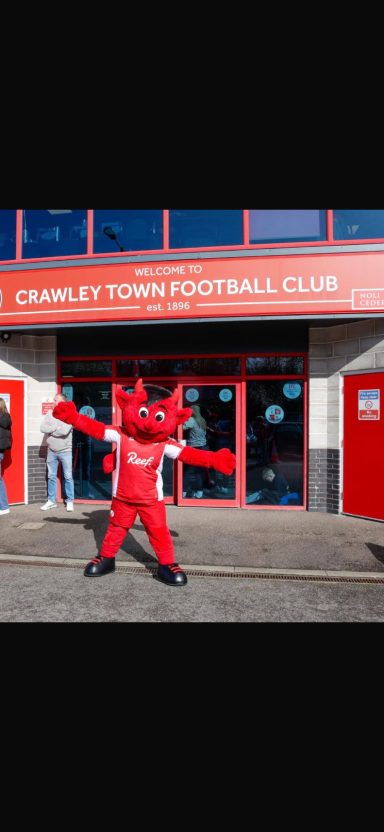 A red mascot posing cheerfully outside Crawley Town Football Club.