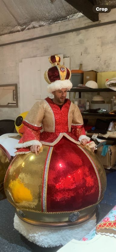 Person wearing a grand crown and costume with a large red and gold bodice.