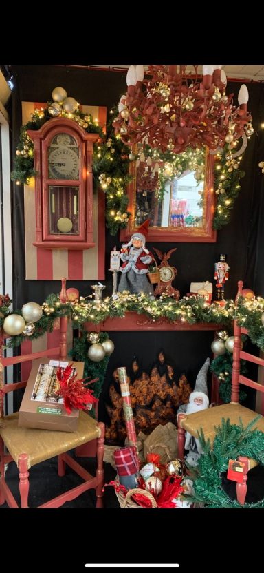 Festive holiday decor with a clock, mirror, and decorated fireplace surrounded by chairs.