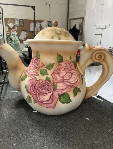 Large decorative teapot with pink roses and green leaves on a light background.
