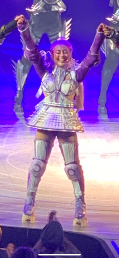 A performer dressed in a metallic costume strikes a celebratory pose on stage.