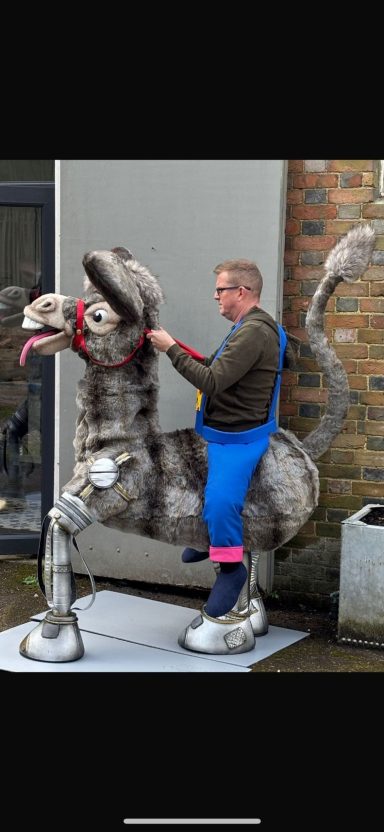A person in blue overalls sits on a metallic horse sculpture.