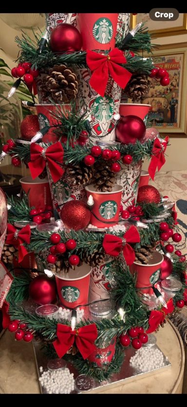 A decorative Christmas tree made of Starbucks cups, adorned with red ornaments and bows.