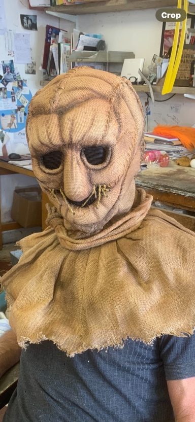 A person wearing a creepy mask with large eyes and a tattered cloak.