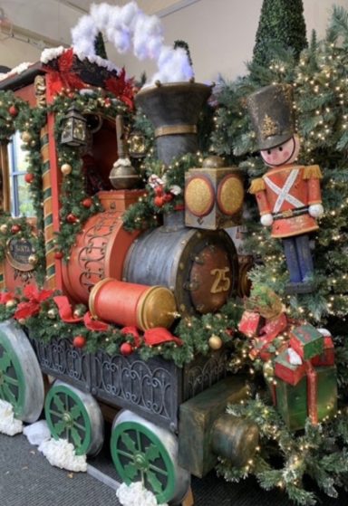 A festive train adorned with greenery, ornaments, and a toy soldier figure.