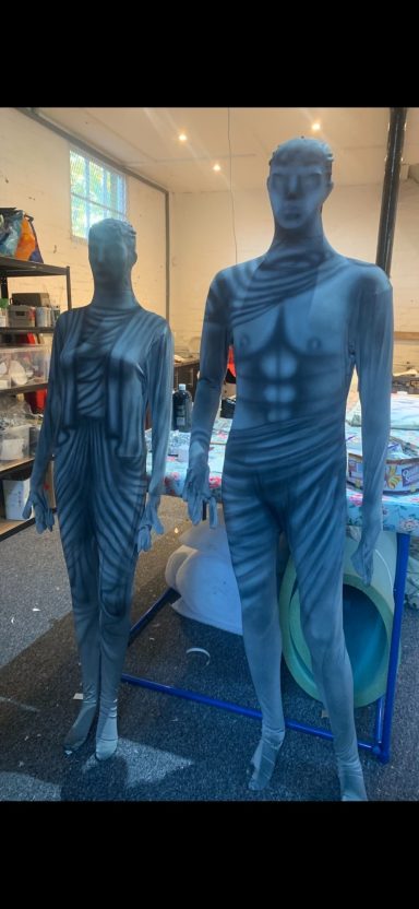 Two grey mannequins in a workshop setting, displaying different poses and clothing styles.