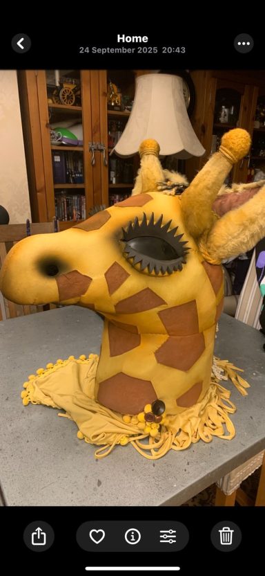 A whimsical giraffe head sculpture with exaggerated features and a yellow-brown pattern.