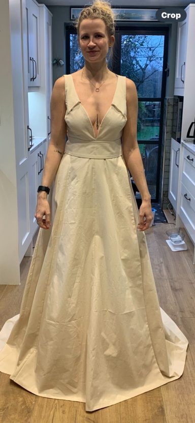 A woman in a stylish cream-coloured evening gown stands in a kitchen.