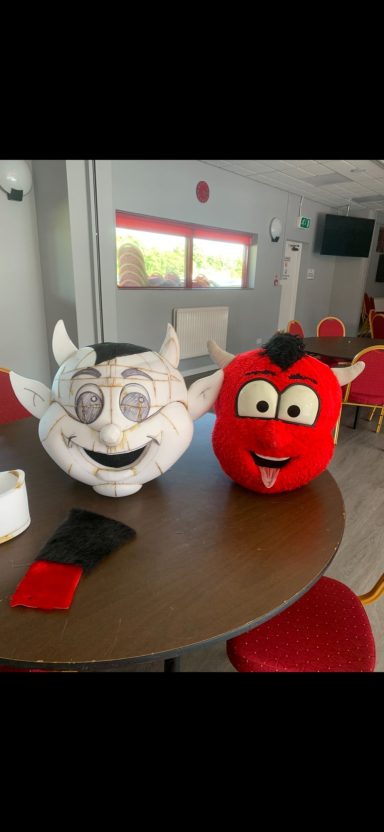 Two cartoonish characters, one grey and one red, with large smiles, sitting on a table.