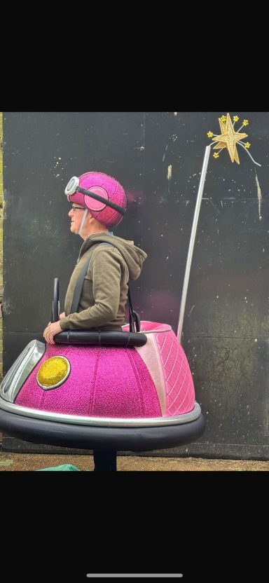 A person in a pink bumper car with a star-shaped antenna, smiling.