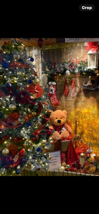 A decorated Christmas tree next to a teddy bear holding a gift.