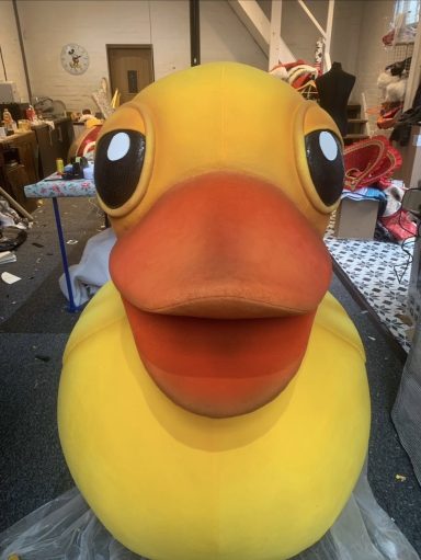 Large, cheerful yellow rubber duck with big eyes and a wide smile in a playful setting.